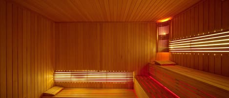 A sauna with wooden walls and benches, featuring red and yellow lighting.