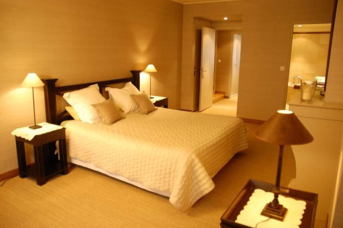 A hotel room with a bed, two bedside tables with lamps, a nightstand, a mirror, and a small table with a decorative item.
