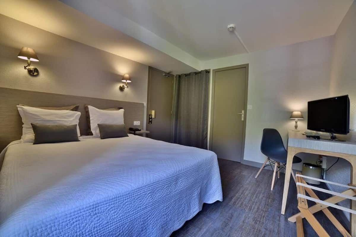 A hotel room with a large bed, a desk with a chair, a television, and a door leading to a bathroom.