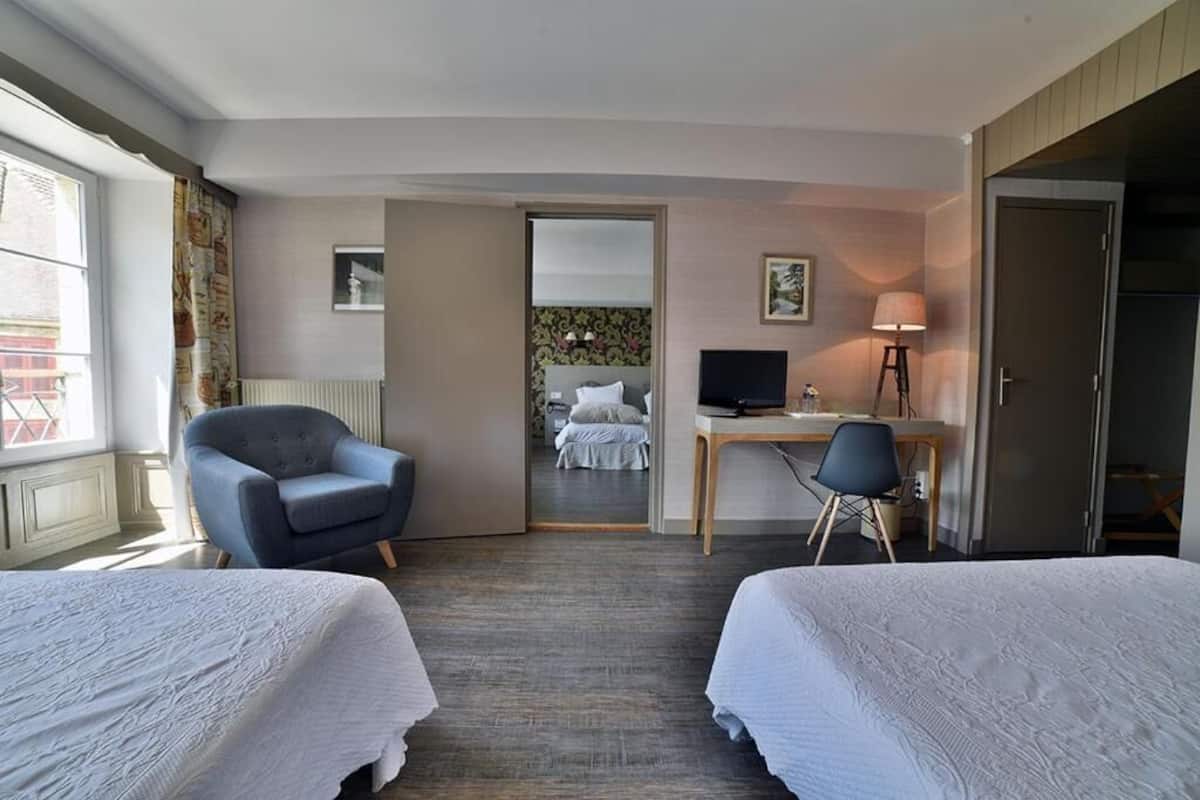 A hotel room with two beds, a desk, a chair, a TV, and a lamp.