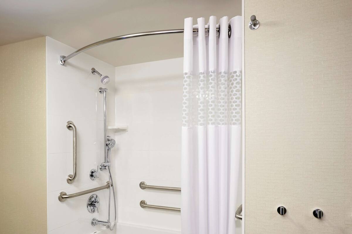 A modern bathroom with a walk-in shower, grab bars, and a white bathtub.