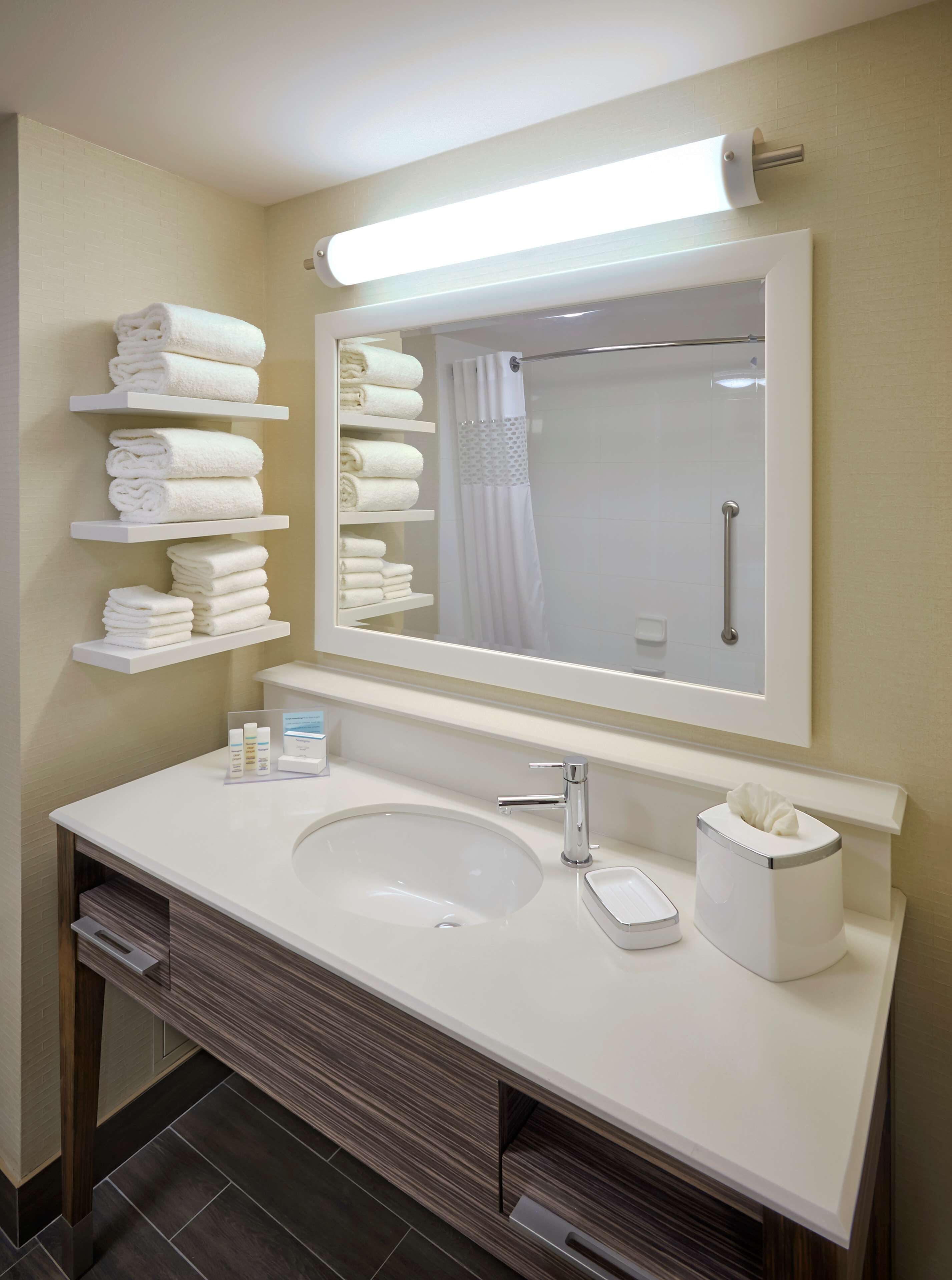 Un baño moderno con tocador blanco, un espejo grande, toallero y zona de ducha.