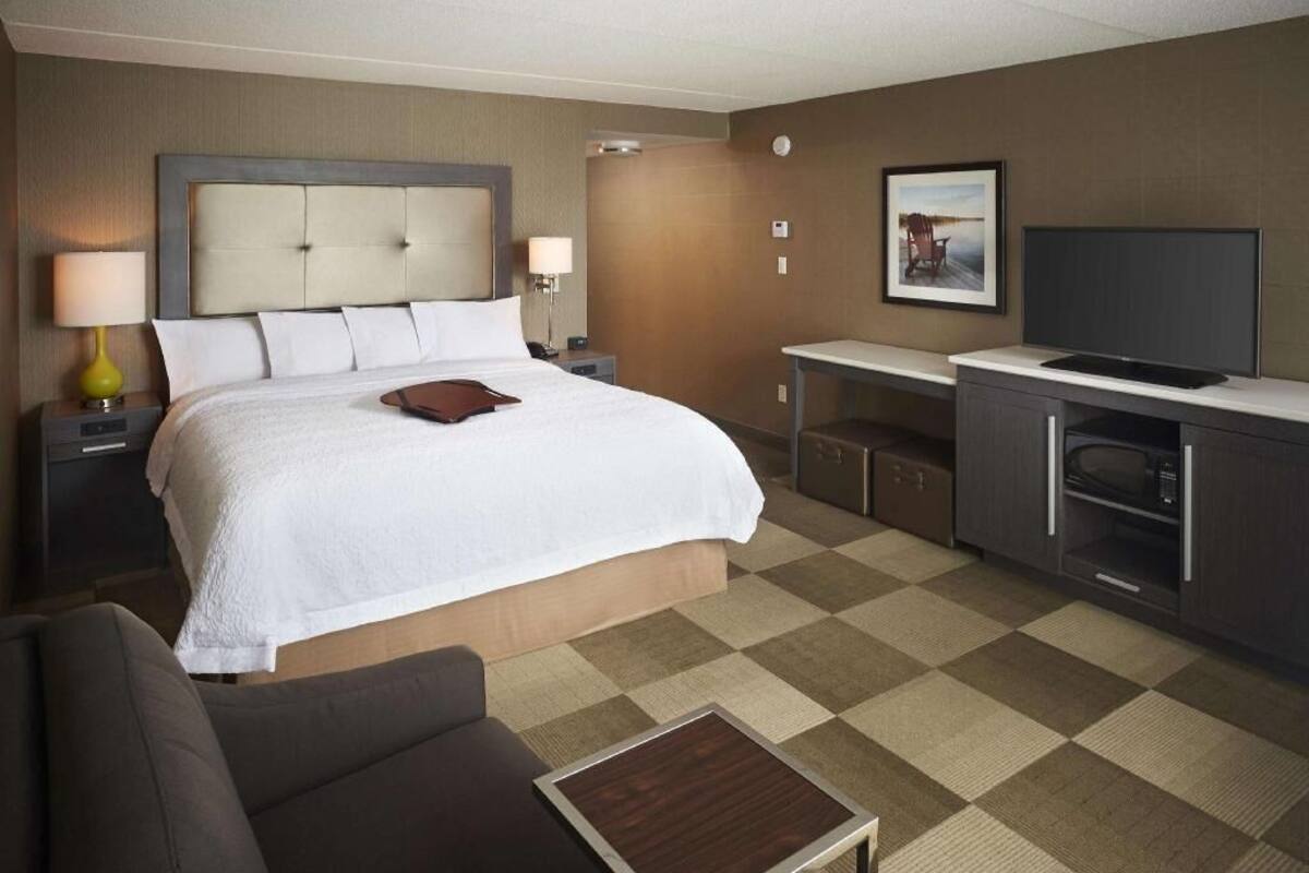 A hotel room with a large bed, bedside tables, a desk, a television, and a microwave.