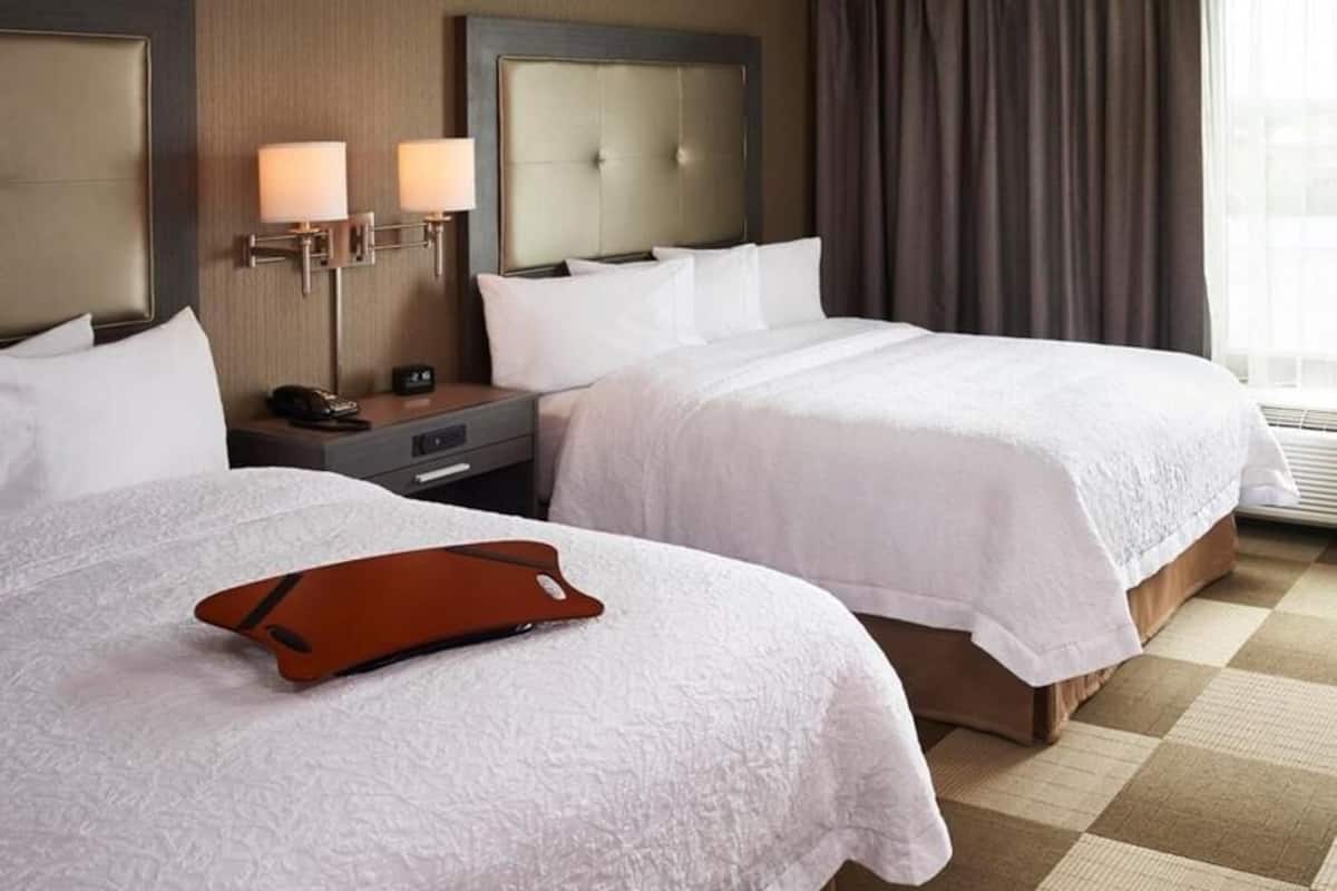 A hotel room with two beds, a nightstand with a lamp, a telephone, and a check-in station.