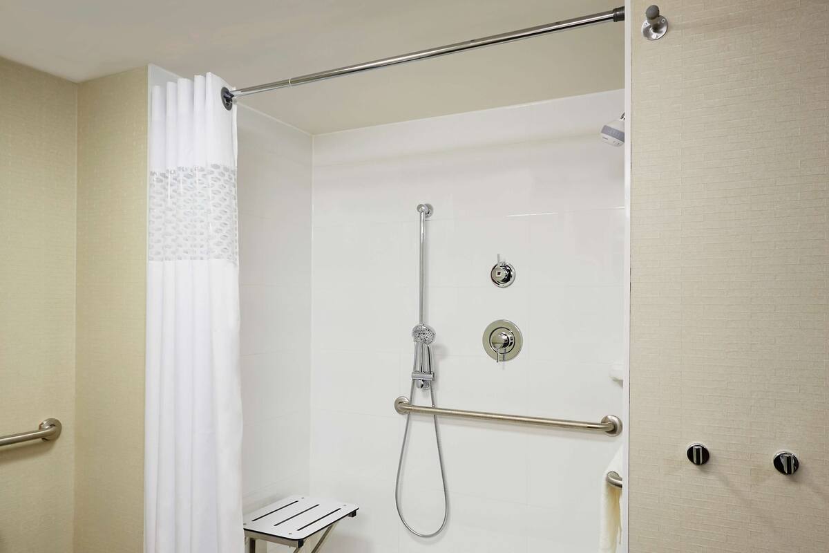 A walk-in shower with a glass door, a white towel rack, and a metal grab bar.