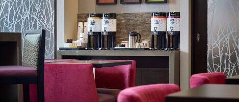 Un café moderno con sillas tapizadas en rojo, una barra de café con varias máquinas de café y obras de arte enmarcadas en la pared.