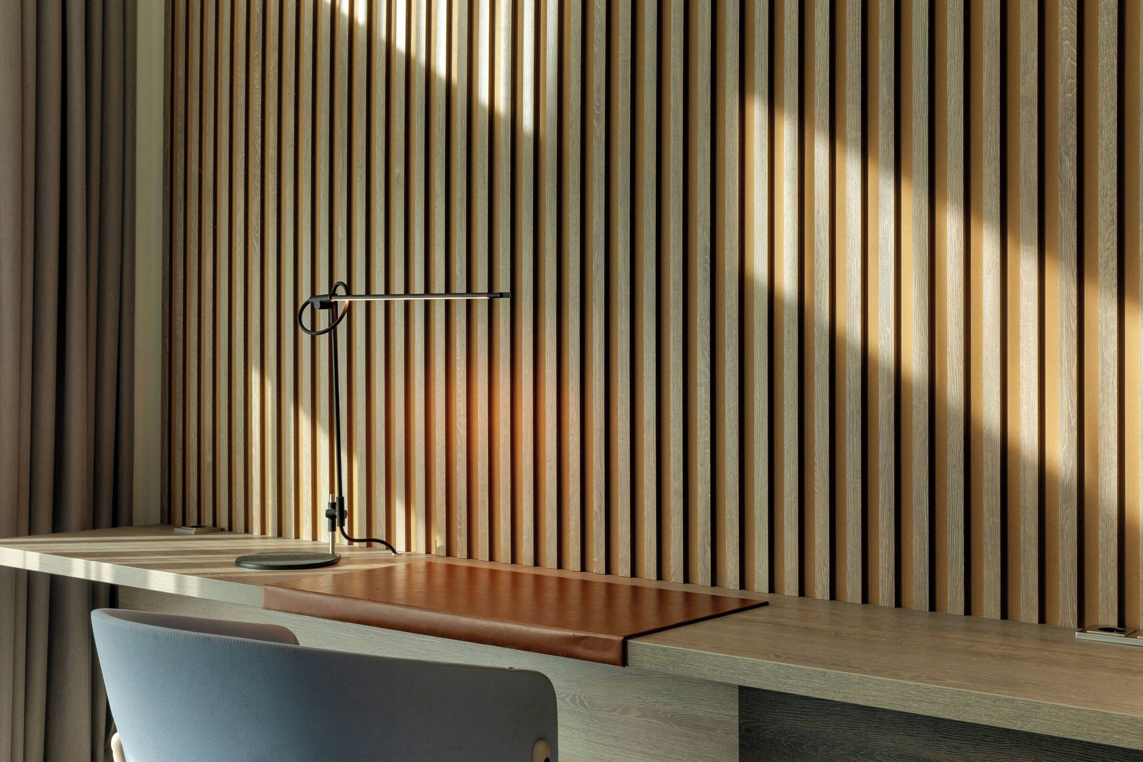 A modern desk with a wooden slat wall behind it.