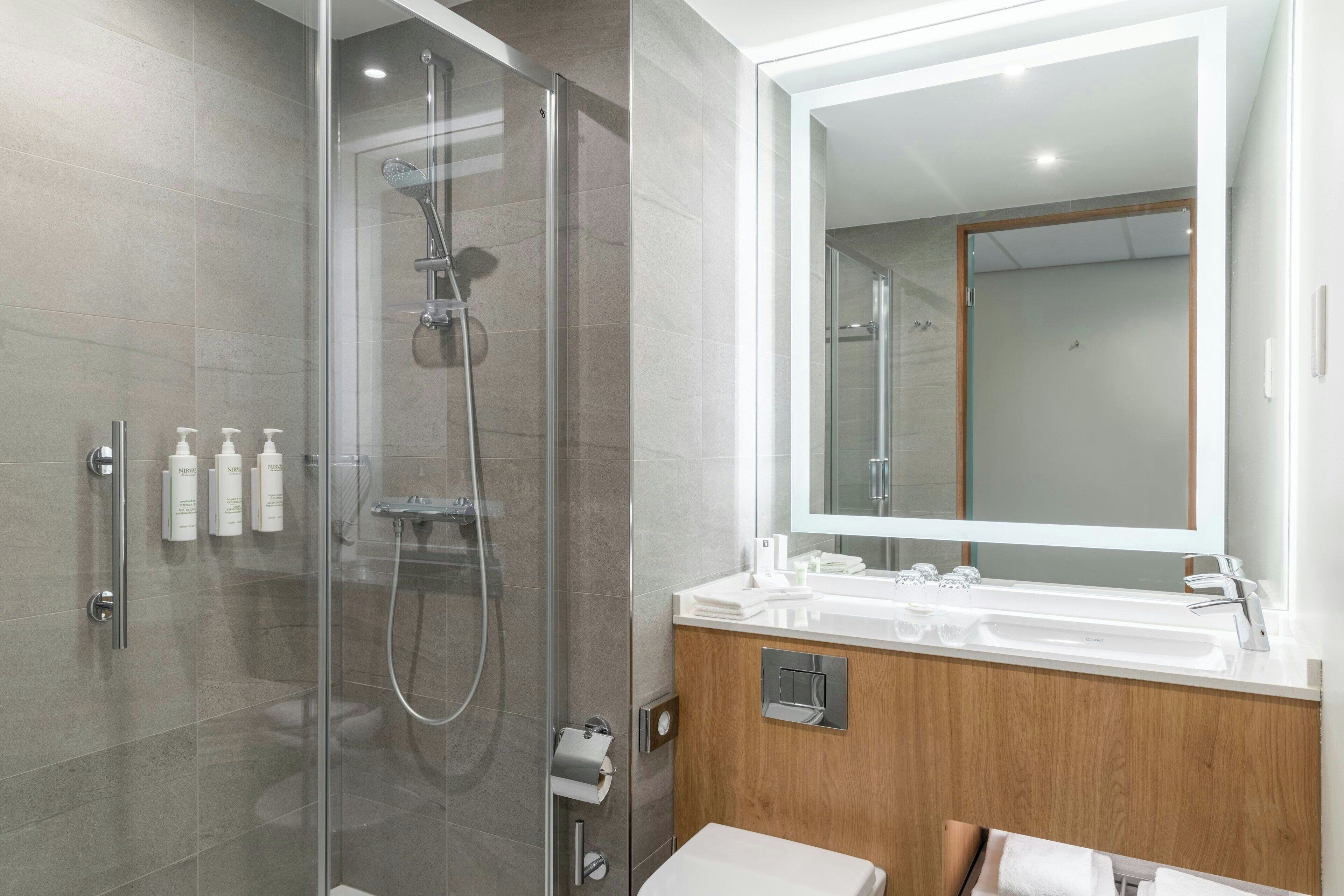 Une salle de bain moderne avec une douche à parois de verre, un meuble-lavabo en bois et un grand miroir.