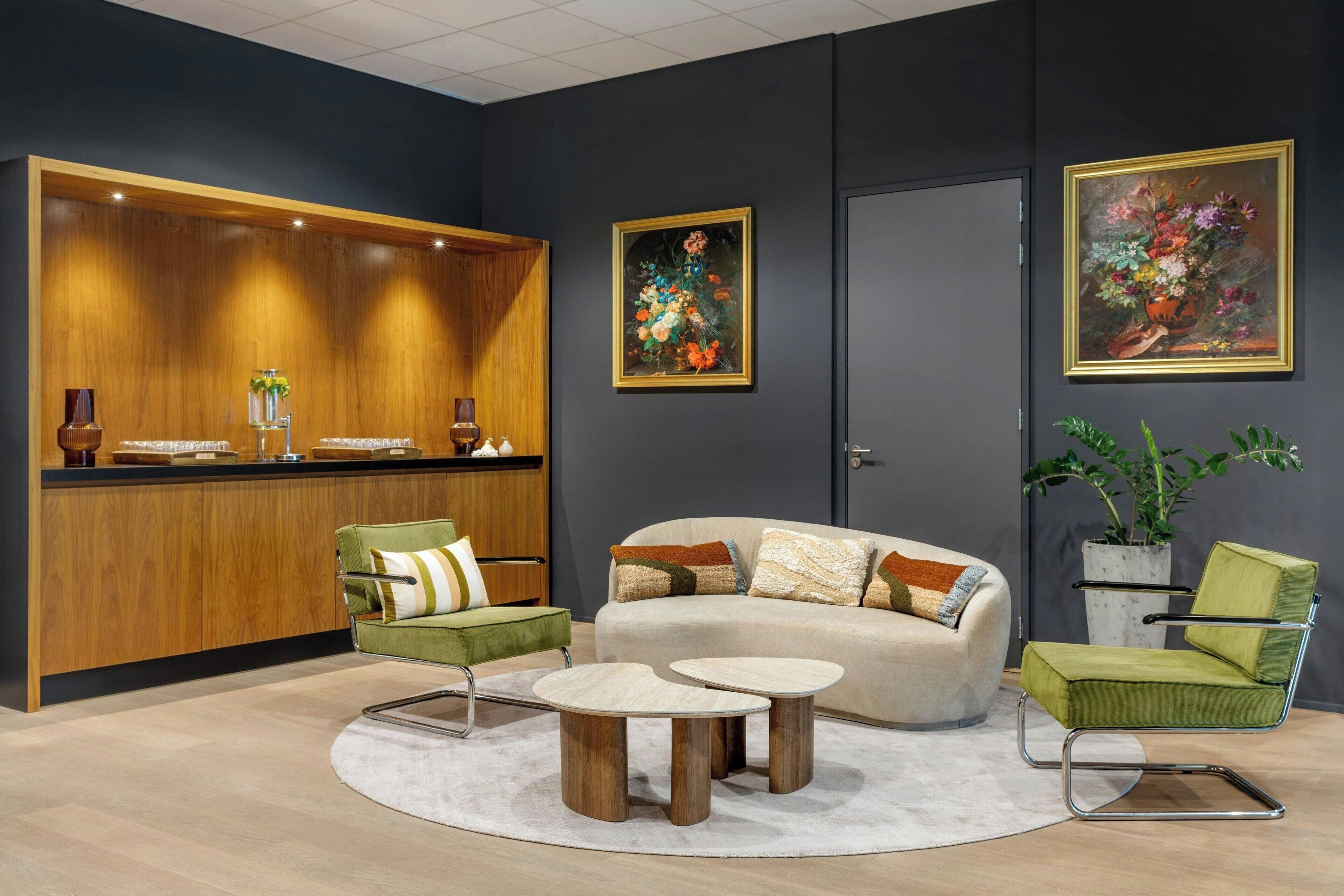 Una zona de recepción moderna con un mostrador de madera, sillones verdes, un sofá beige y dos mesas redondas.