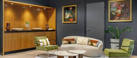 Una zona de recepción moderna con un mostrador de madera, sillones verdes, un sofá beige y dos mesas redondas.