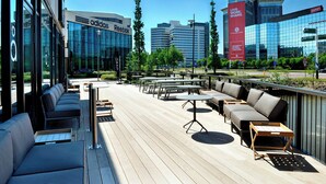 Un espacio al aire libre con sofás y mesas, con vistas a un edificio moderno con ventanas de vidrio y un letrero rojo.