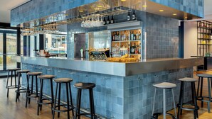 Zona de bar con paredes de azulejos azules, una vitrina de vidrio y varios taburetes.