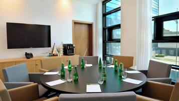 Un salón de conferencias con una amplia pantalla plana, una máquina de café y una mesa preparada para reuniones.