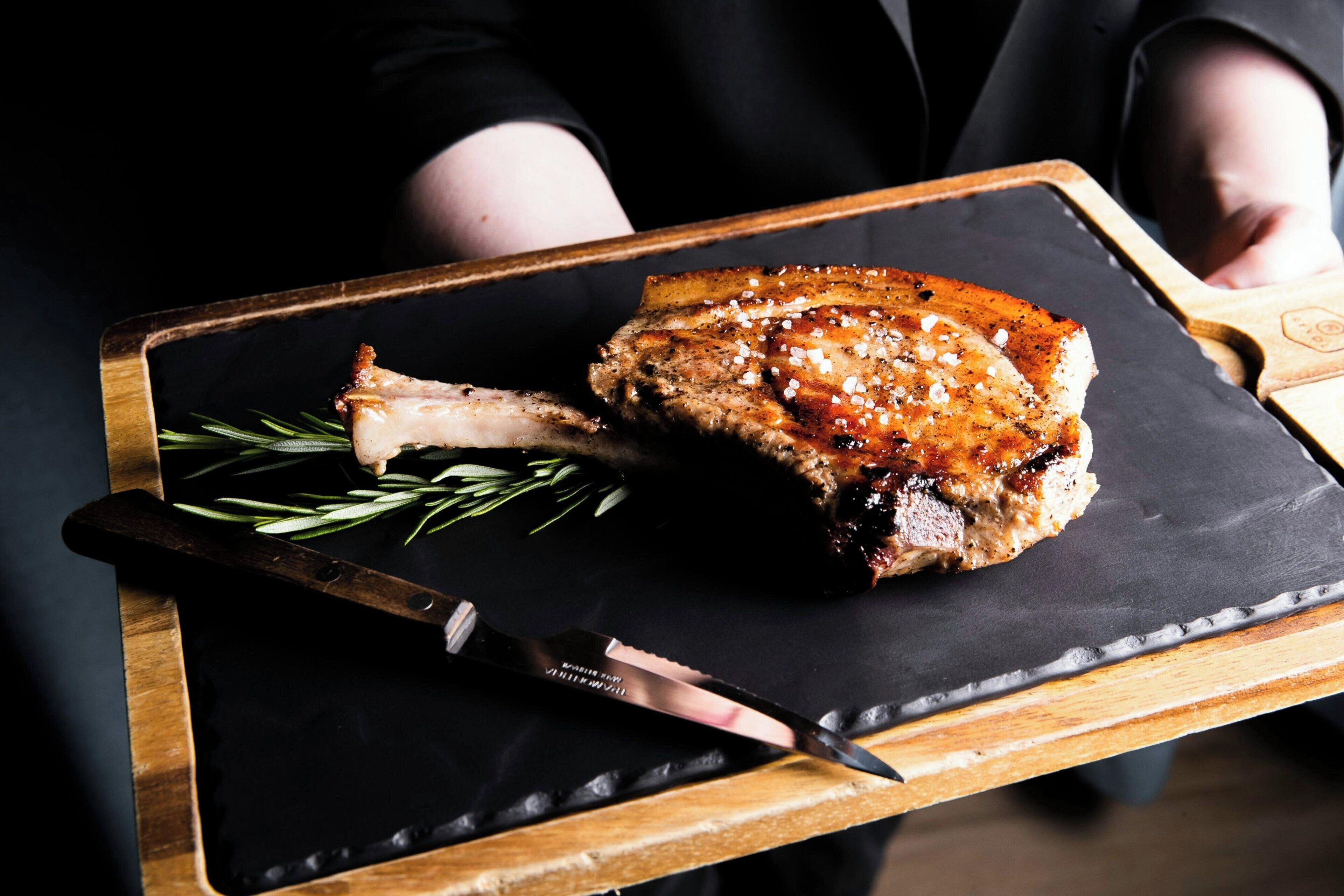 Une personne portant un plateau sur lequel se trouve un plat de viande rôtie et un couteau.