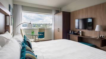 Habitación de hotel con una cama grande, un escritorio con silla, televisión y ventana con vista a la ciudad.