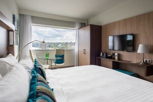 Habitación de hotel con una cama grande, un escritorio con silla, televisión y ventana con vista a la ciudad.
