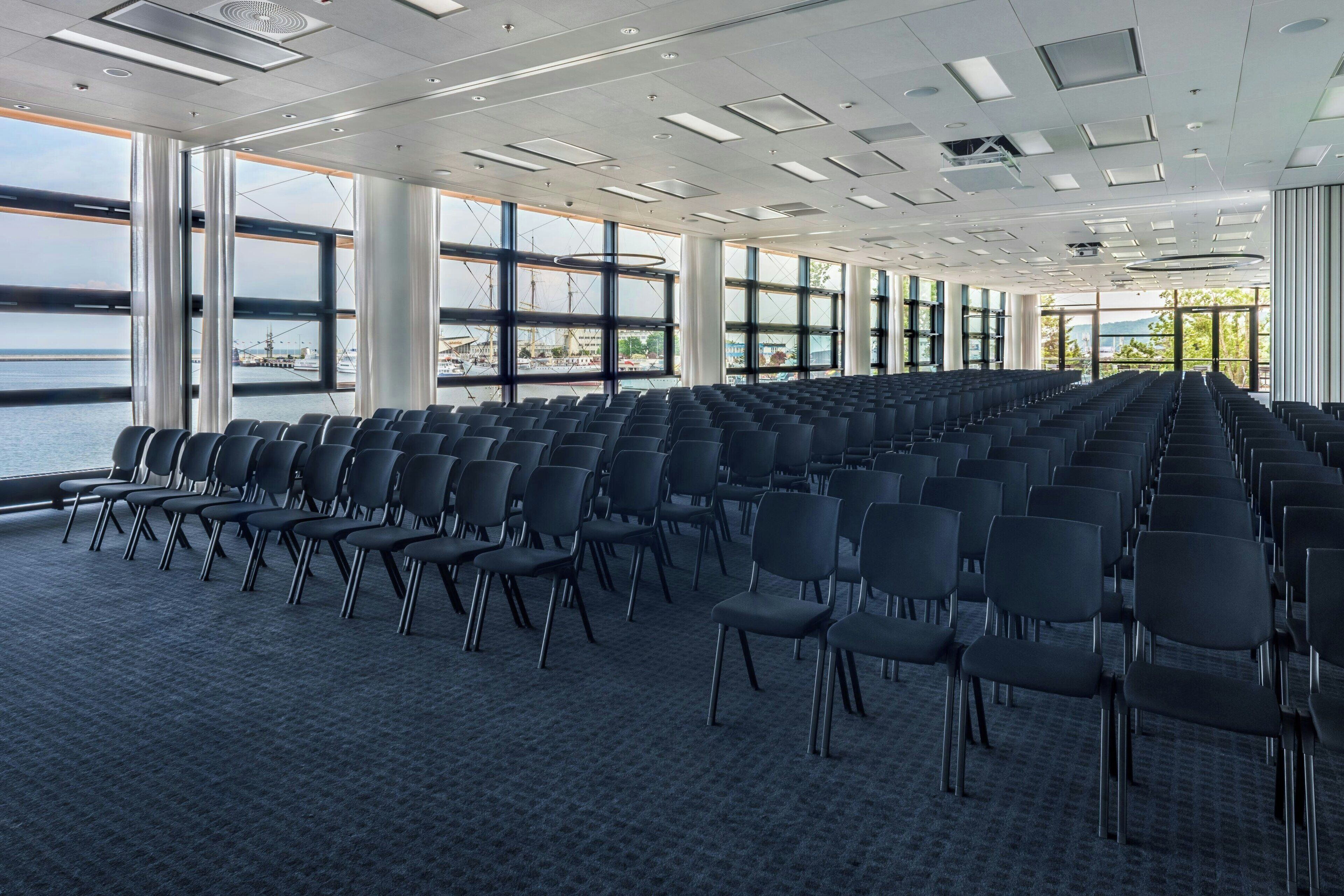 A conference room with rows of chairs, large windows, and a view of the sea.