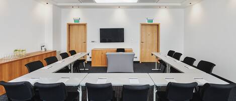 A conference room with a long table, black chairs, a podium, and a TV screen.