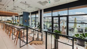 A modern indoor dining area with a long counter, wooden chairs, and large windows offering a view of a marina.