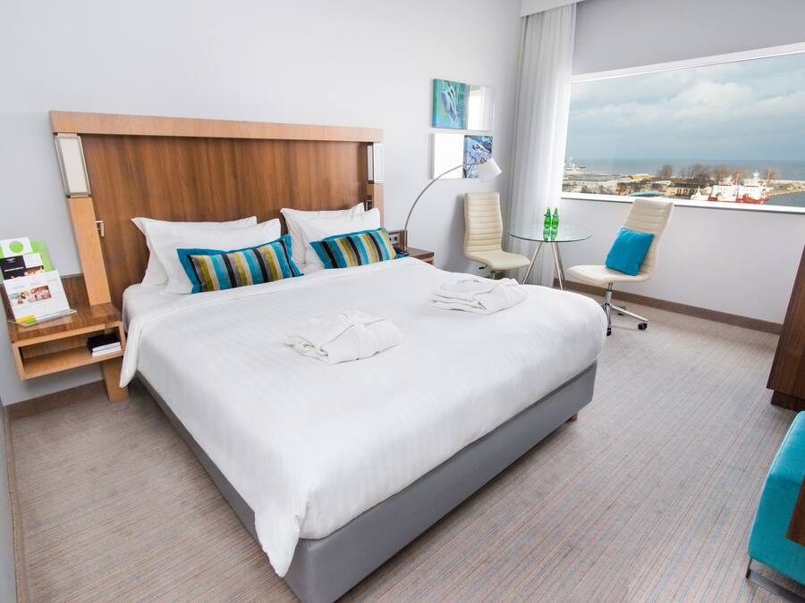 Une chambre d’hôtel avec un grand lit, un bureau, une chaise et une vue sur la mer.