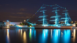 A large ship with multiple masts and a modern building nearby.