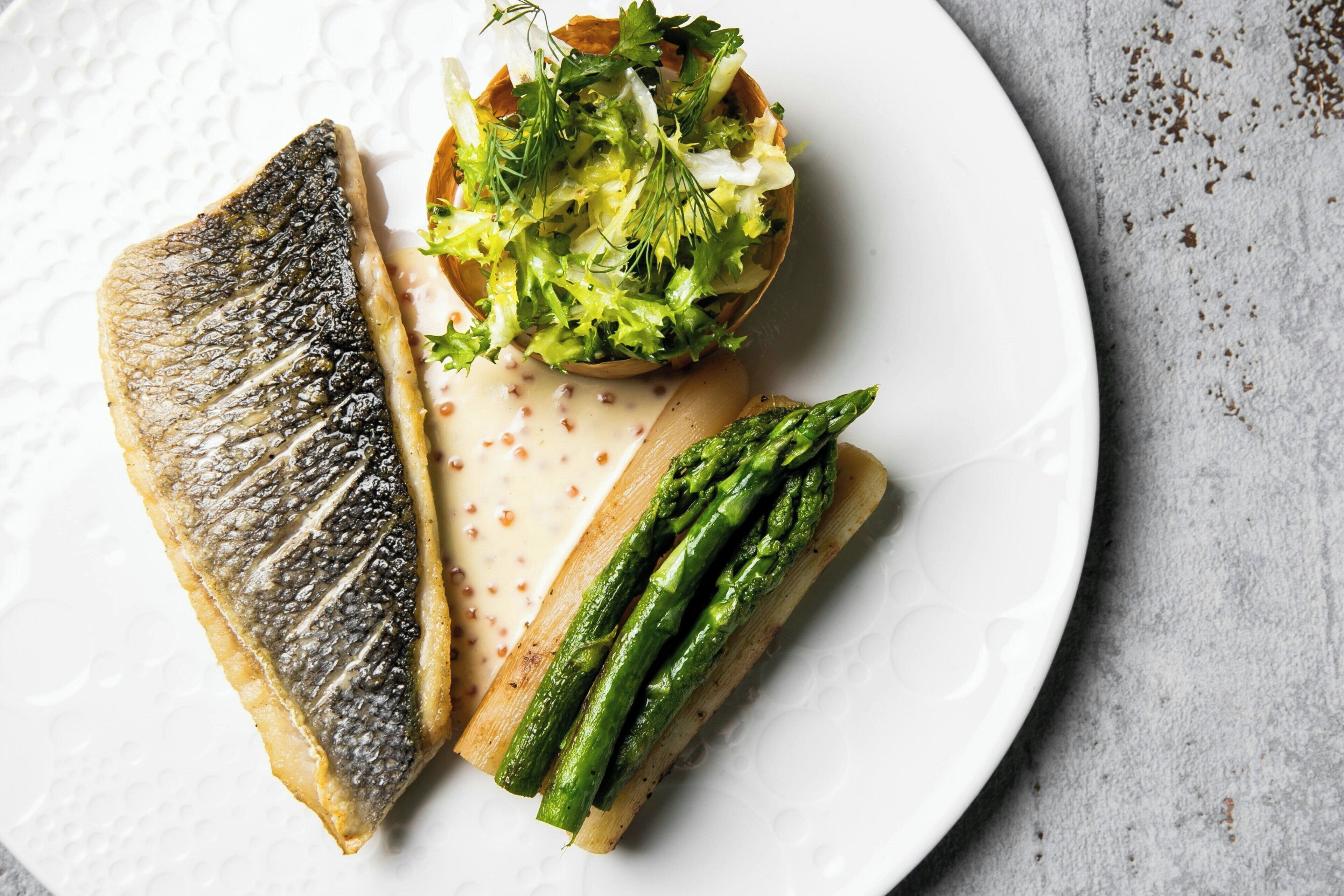 A plate with grilled fish, asparagus, and a salad.