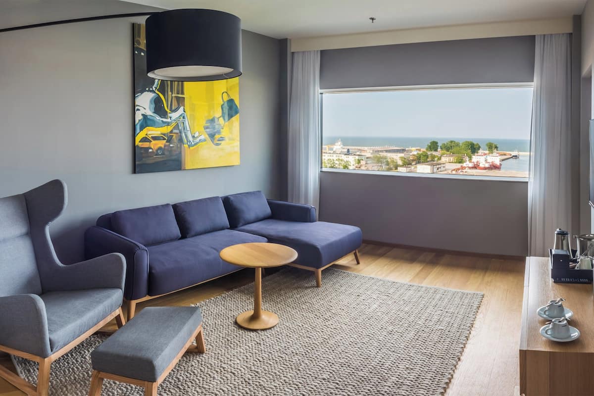 A modern living room with a sofa, armchairs, a coffee table, and a large window offering a city view.