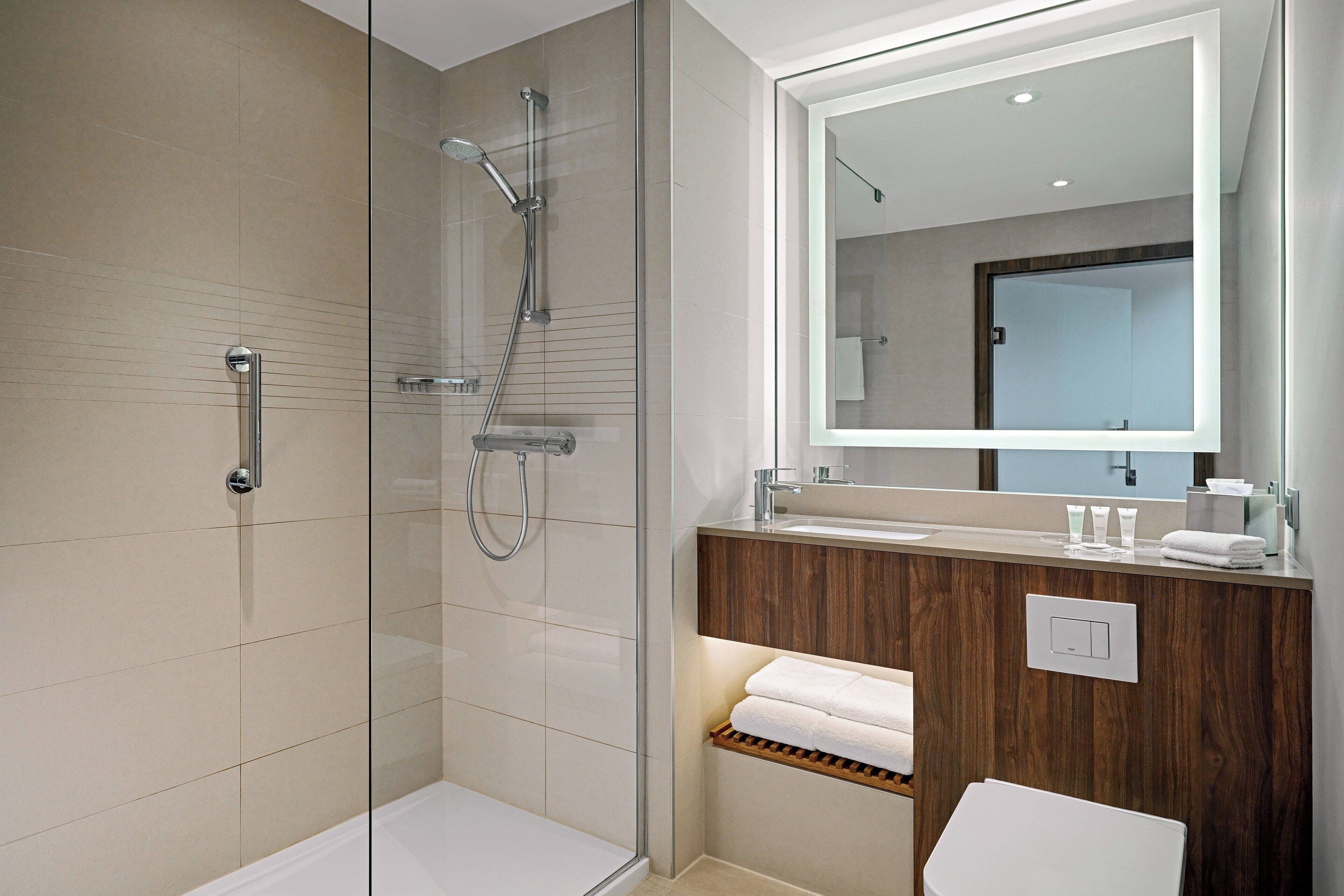 A modern bathroom with a glass-enclosed shower, a wooden vanity, and a large mirror.
