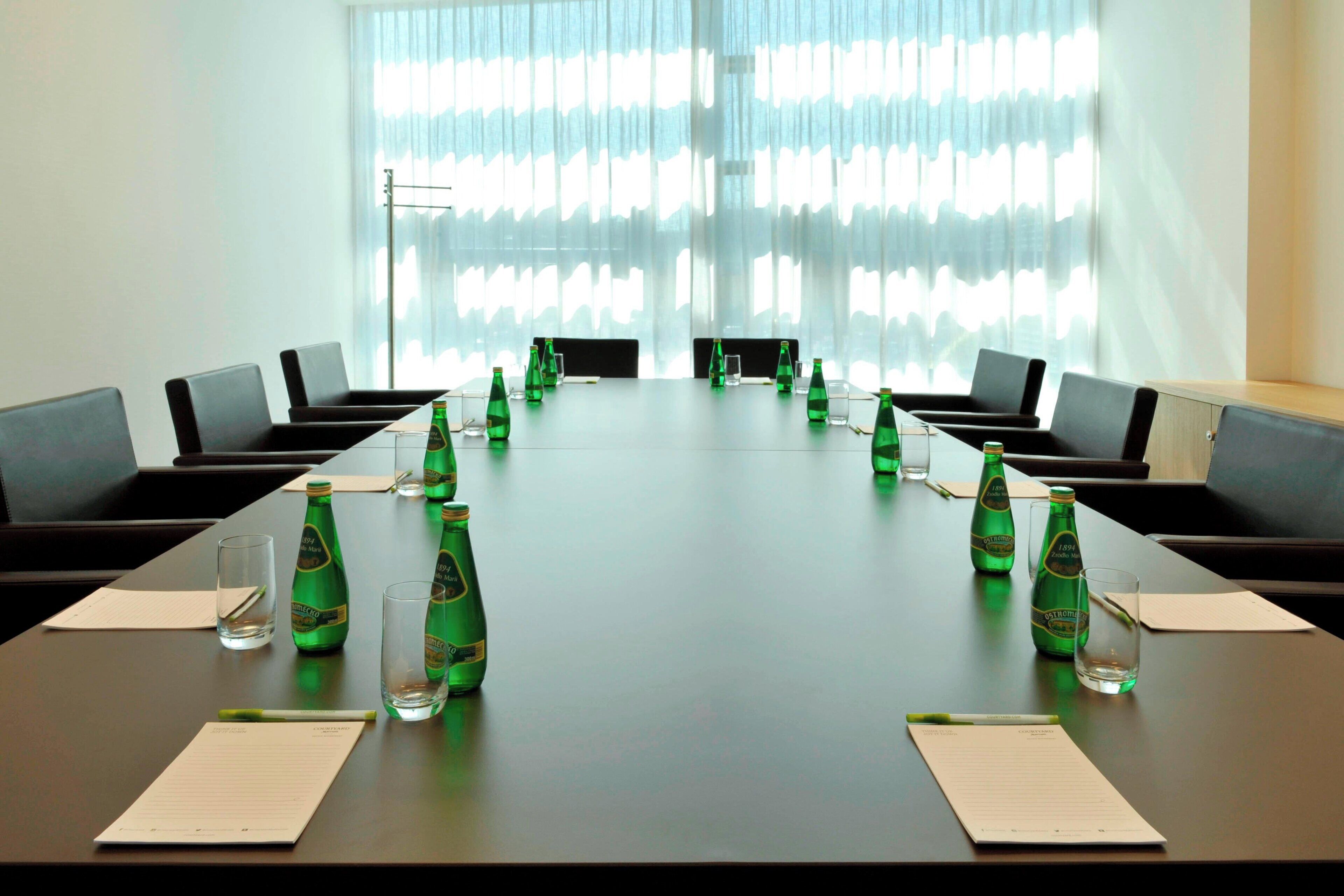 Une salle de conférence avec une longue table, des chaises et des bouteilles vertes.