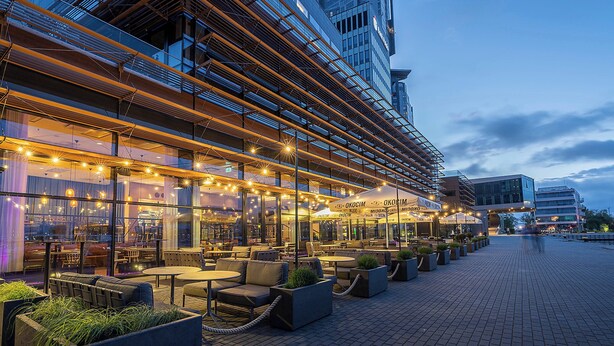 An outdoor seating area with tables and chairs, a modern building with glass windows, and a clear sky.