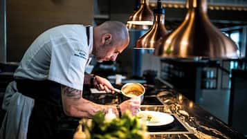 Um chef prepara comida em uma cozinha moderna com luminárias pendentes de cobre e bancada de mármore.