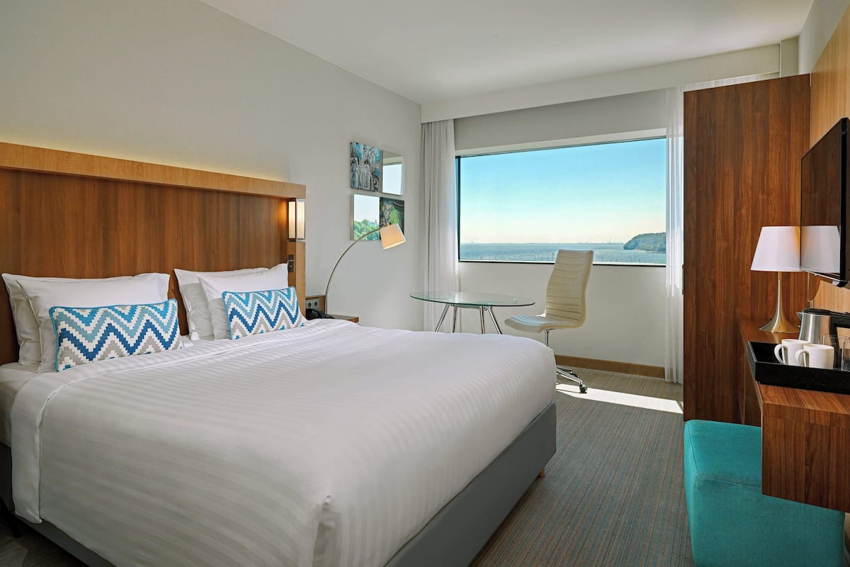 A hotel room with a large bed, a desk, a chair, and a view of the ocean.