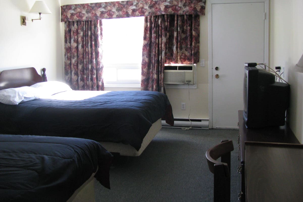 A hotel room with a bed, a chair, a television, and an air conditioning unit.