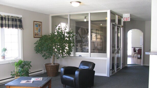 A room with a large window, a potted plant, a leather chair, a wooden table, and an exit sign. - Prospect Inn (Fredericton)