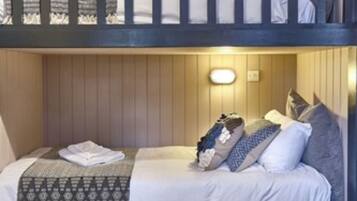 Une chambre avec un lit superposé, un plancher en bois, un petit tapis et un luminaire fixé au mur.