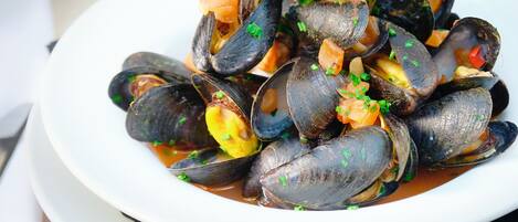 A plate of mussels garnished with herbs, a glass of white wine, and a potted plant in the background.