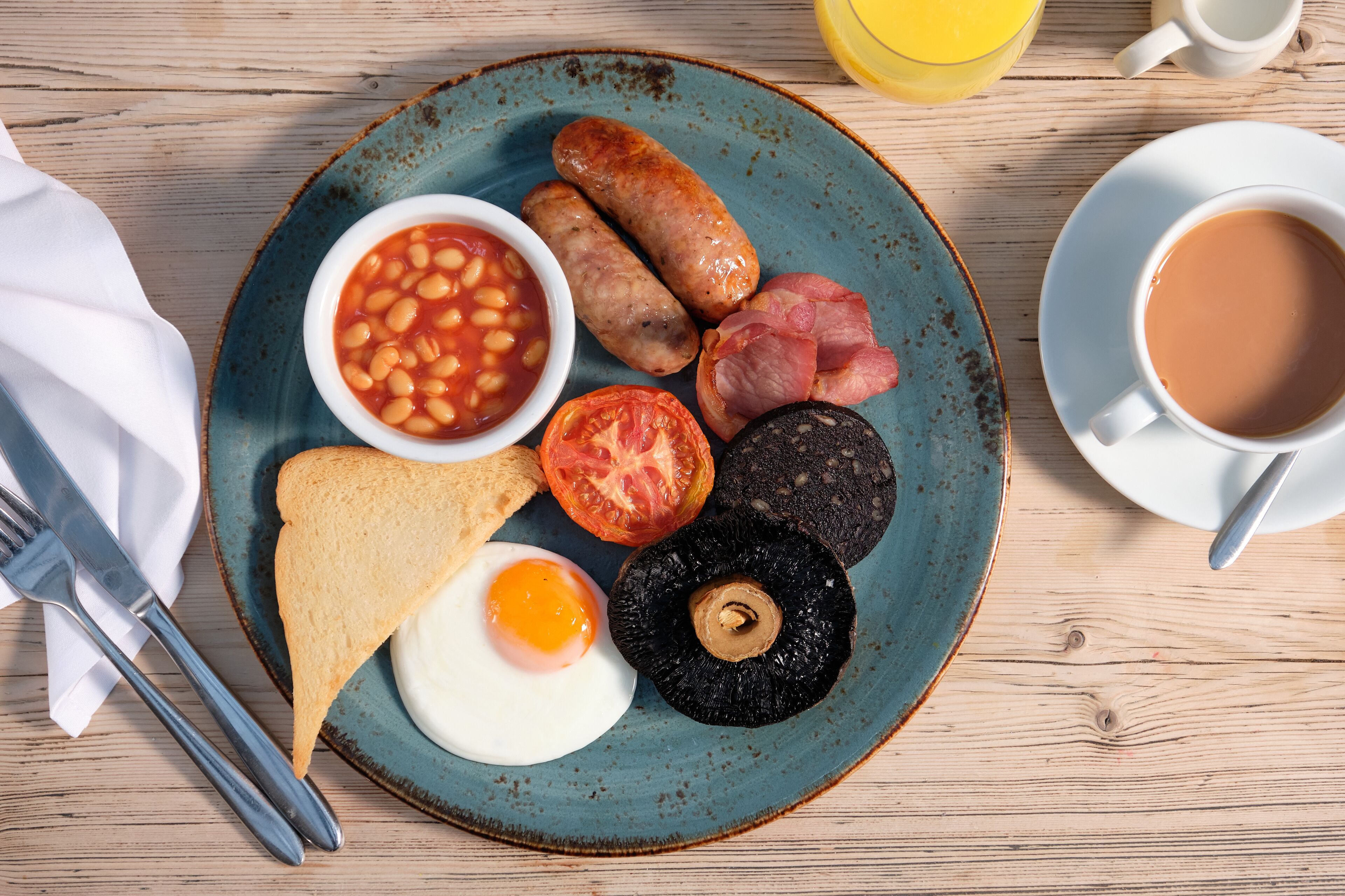 Un plato de desayuno con frijoles, salchichas, tocino, tomate, hongo, tostadas y un huevo frito.