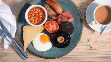 Un plato de desayuno con frijoles, salchichas, tocino, tomate, hongo, tostadas y un huevo frito.