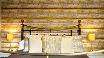 A bed with a metal frame and a wooden headboard against a rustic wall. There are two bedside lamps and a white nightstand.