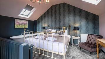 A bedroom with a sloped ceiling, a bed with a metal frame, a radiator, a small table, a chair, and a painting on the wall.