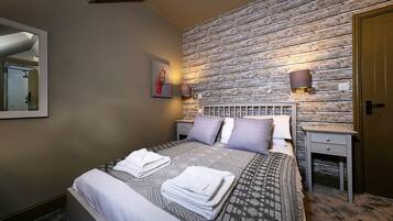 A neatly made bed with folded towels, a wooden textured wall, and a small bedside table with a lamp.