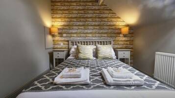 Un dormitorio con una colcha estampada, dos mesitas de noche con lámparas y una escalera que conduce a un piso superior.