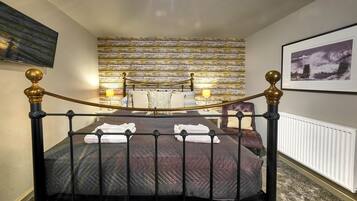 Een net opgemaakt bed met een donge deken, twee bedlampjes en een aan de muur bevestigd fotolijstje.