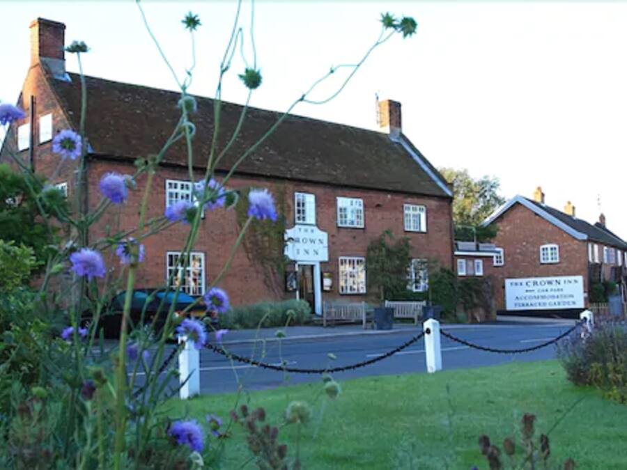 Un edificio de ladrillo tradicional con un letrero que dice 'The Crown Inn' y 'The Crown Inn Alojamiento y Jardines para Autocaravanas'.