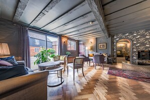 Una habitación acogedora y bien iluminada con pisos de madera, un ventanal grande y un espacio de descanso con sofá y sillones.