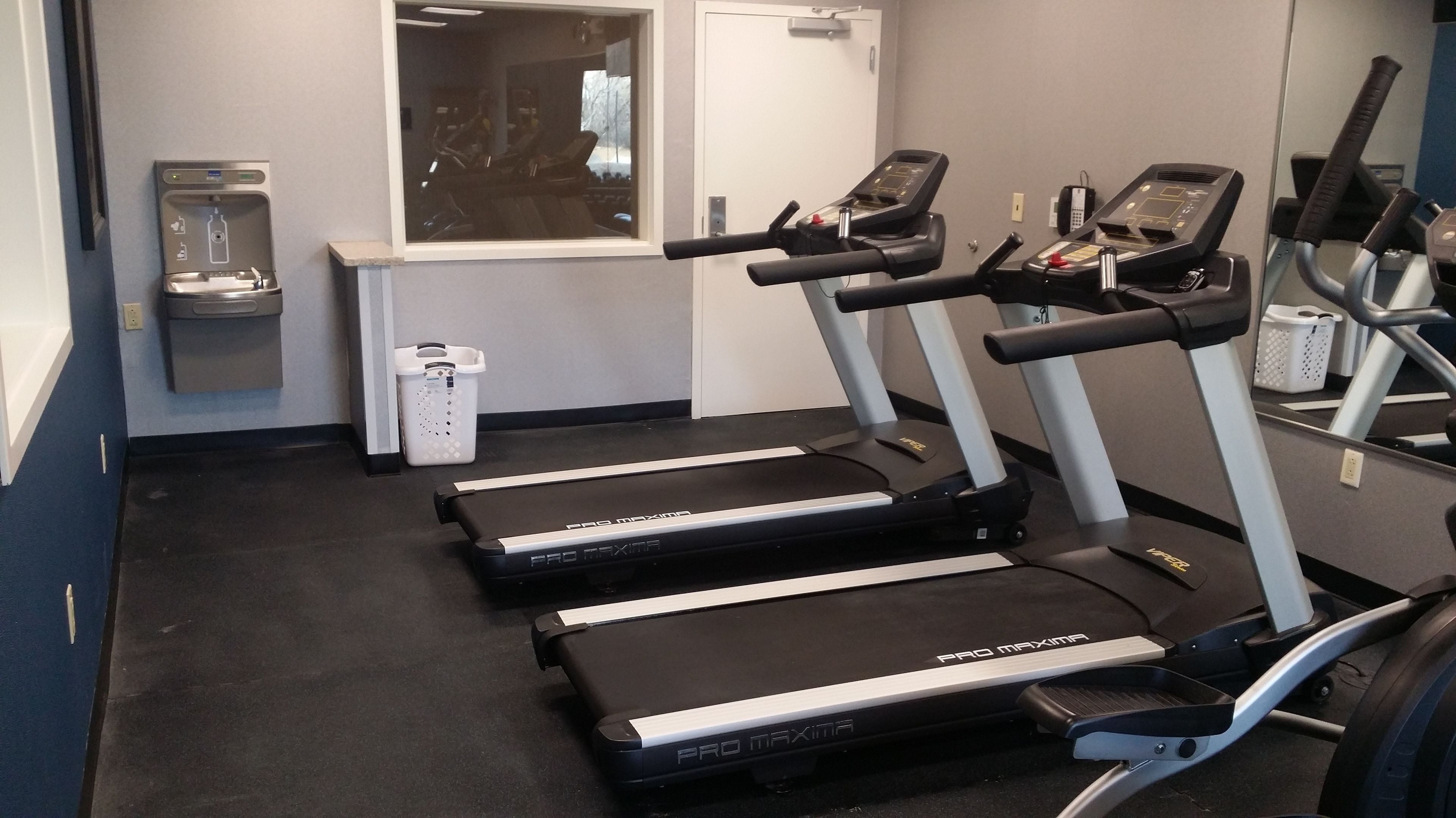 A fitness room with treadmills, a water dispenser, and a trash bin.