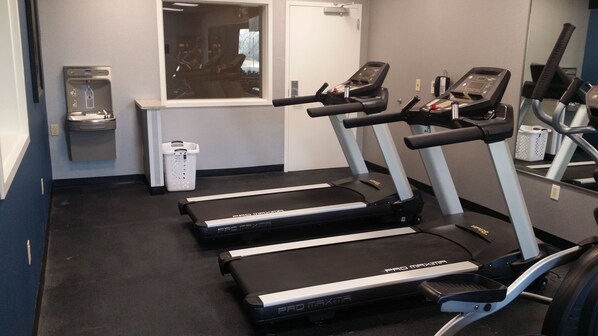 A fitness room with treadmills, a water dispenser, and a trash bin.