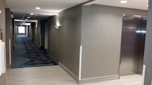 Stylish corridor with patterned carpet leading to elevator and recessed lighting.