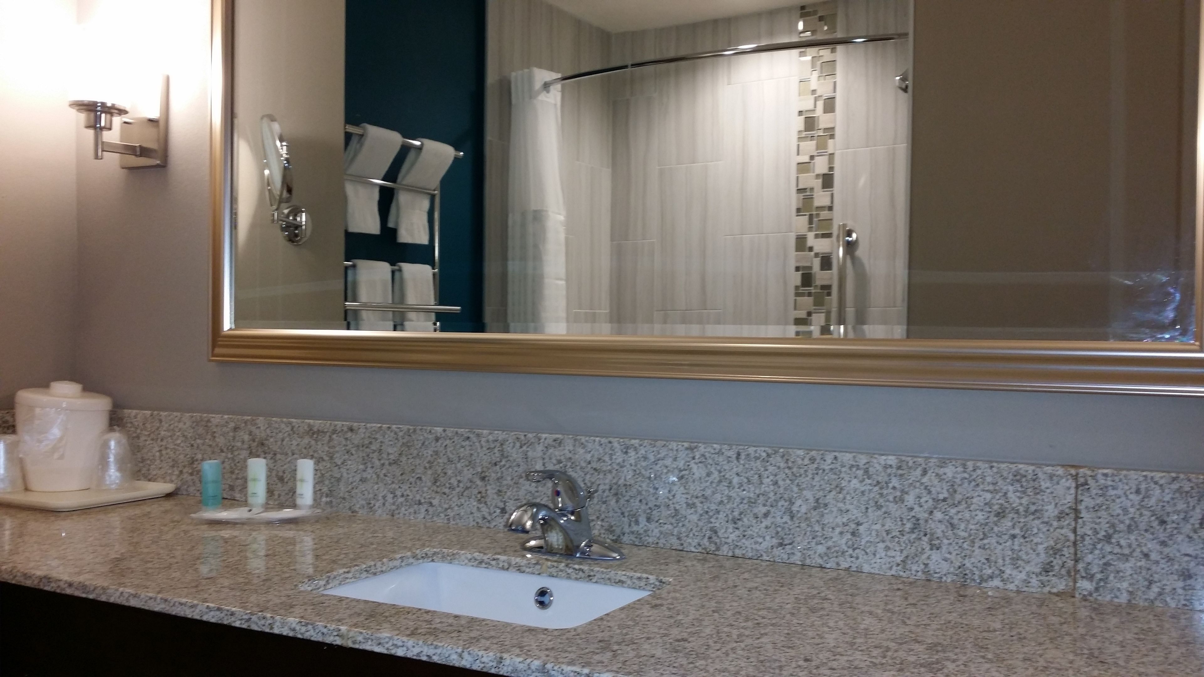 Un baño con encimera de granito, un lavabo, un espejo y zona de ducha.
