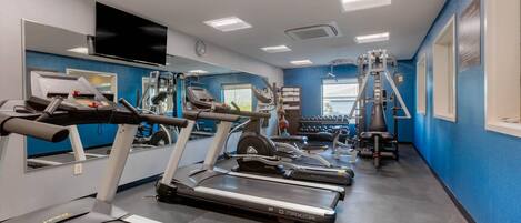 A gym with treadmills, weight machines, and a mirror wall.